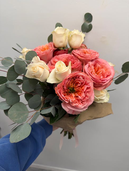 A bouquet of fresh flowers consisting of large, ruffled pink ranunculus and creamy white roses, accented with sprigs of eucalyptus leaves with rounded, silvery-green foliage. The flowers are arranged
