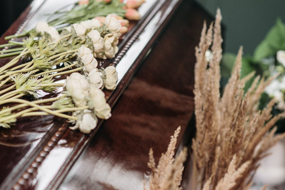 A close-up view of a floral arrangement featuring delicate white roses with slightly opened petals and light green stems, resting on a polished wooden surface. The roses are arranged in a single row a